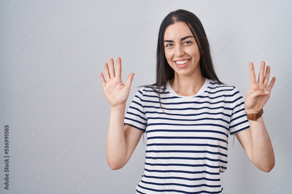 Young brunette woman wearing striped t shirt showing and pointing up with fingers number nine while smiling confident and happy. Young brunette woman wearing striped t shirt showing and pointing up with fingers number nine while smiling confident and happy.