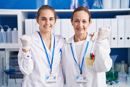 Two women working at scientist laboratory screaming proud, celebrating victory and success very excited with raised arms