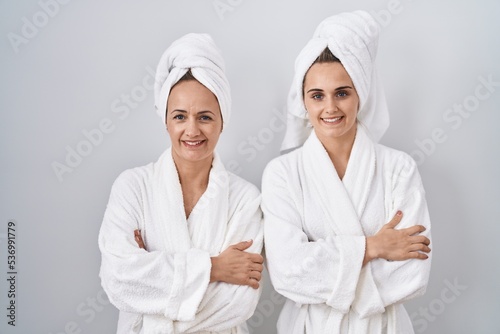 Middle age woman and daughter wearing white bathrobe and towel happy face smiling with crossed arms looking at the camera. positive person.