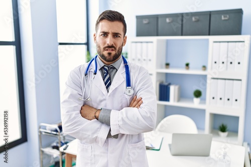 Handsome hispanic man wearing doctor uniform and stethoscope at medical clinic skeptic and nervous, disapproving expression on face with crossed arms. negative person.