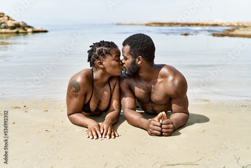 Young african american tourist couple wearing swimwear lying on the sand at the beach.