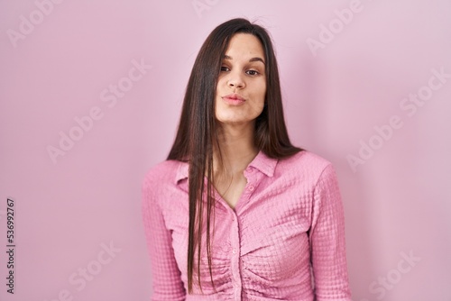 Young hispanic woman standing over pink background looking at the camera blowing a kiss on air being lovely and sexy. love expression. © Krakenimages.com
