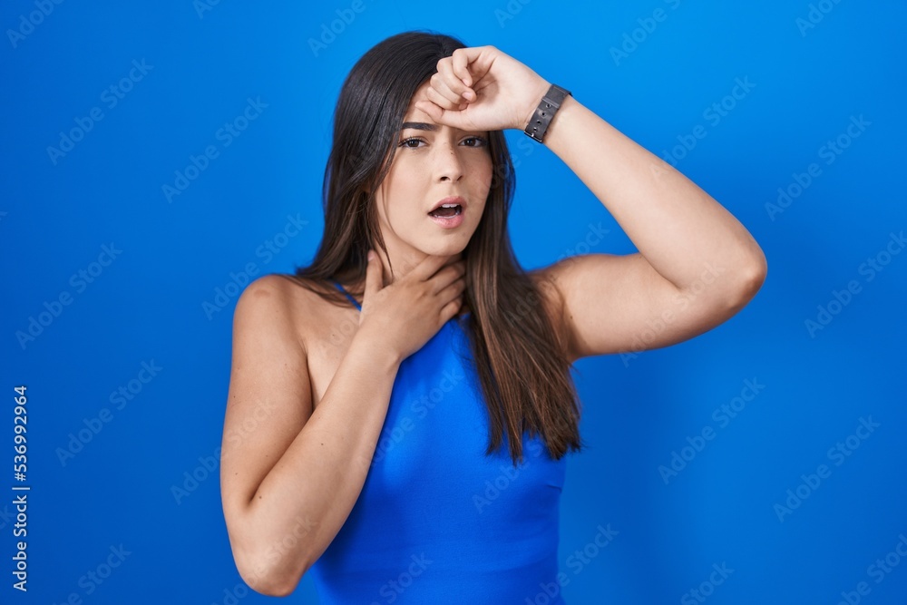 Hispanic woman standing over blue background touching forehead for illness and fever, flu and cold, virus sick Hispanic woman standing over blue background touching forehead for illness and fever, flu and cold, virus sick