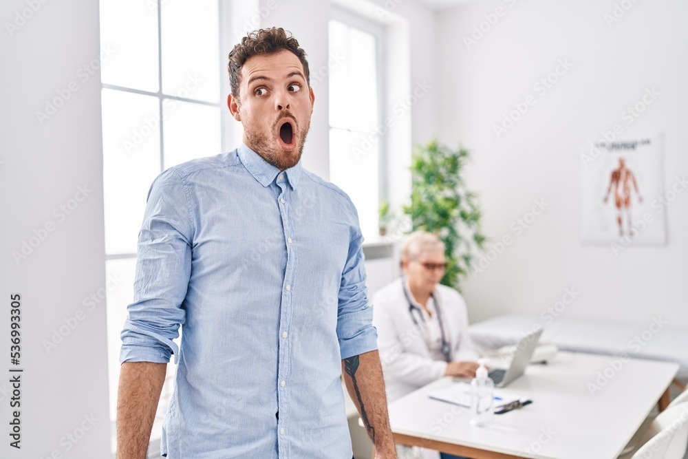 Hispanic man at doctor clinic scared and amazed with open mouth for surprise, disbelief face Hispanic man at doctor clinic scared and amazed with open mouth for surprise, disbelief face
