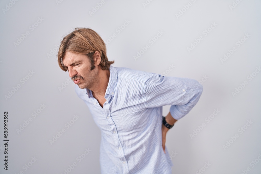 Caucasian man with mustache standing over white background suffering of backache, touching back with hand, muscular pain