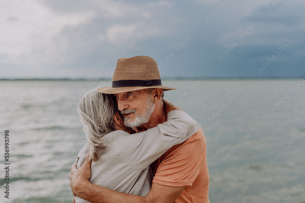 Senior couple in love embracing each other, having romantic moment near the autumn sea.