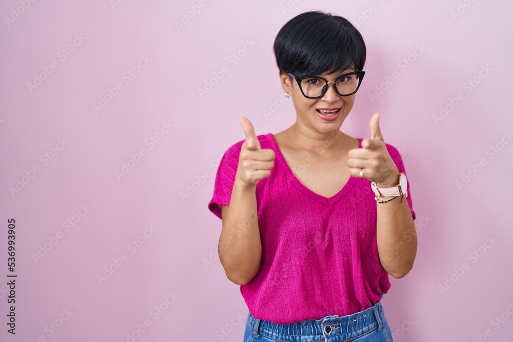 Young asian woman with short hair standing over pink background pointing fingers to camera with happy and funny face. good energy and vibes. Young asian woman with short hair standing over pink background pointing fingers to camera with happy and funny face. good energy and vibes.