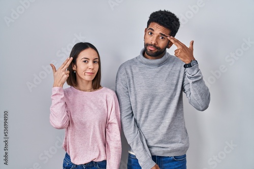 Young hispanic couple standing together shooting and killing oneself pointing hand and fingers to head like gun, suicide gesture.