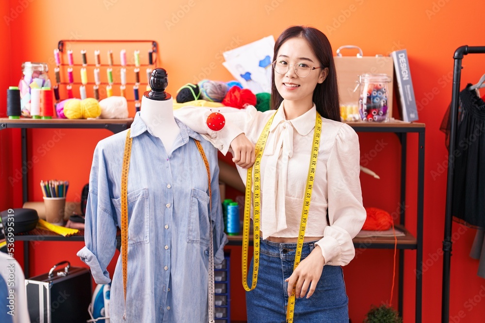 Young chinese woman tailor smiling confident leaning on manikin at atelier