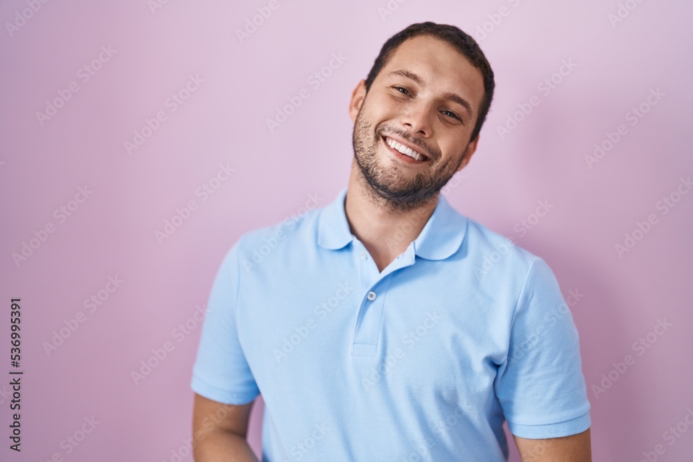 Hispanic man standing over pink background with hands together and crossed fingers smiling relaxed and cheerful. success and optimistic Hispanic man standing over pink background with hands together and crossed fingers smiling relaxed and cheerful. success and optimistic