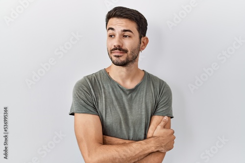 Young hispanic man with beard wearing casual t shirt over white background smiling looking to the side and staring away thinking.