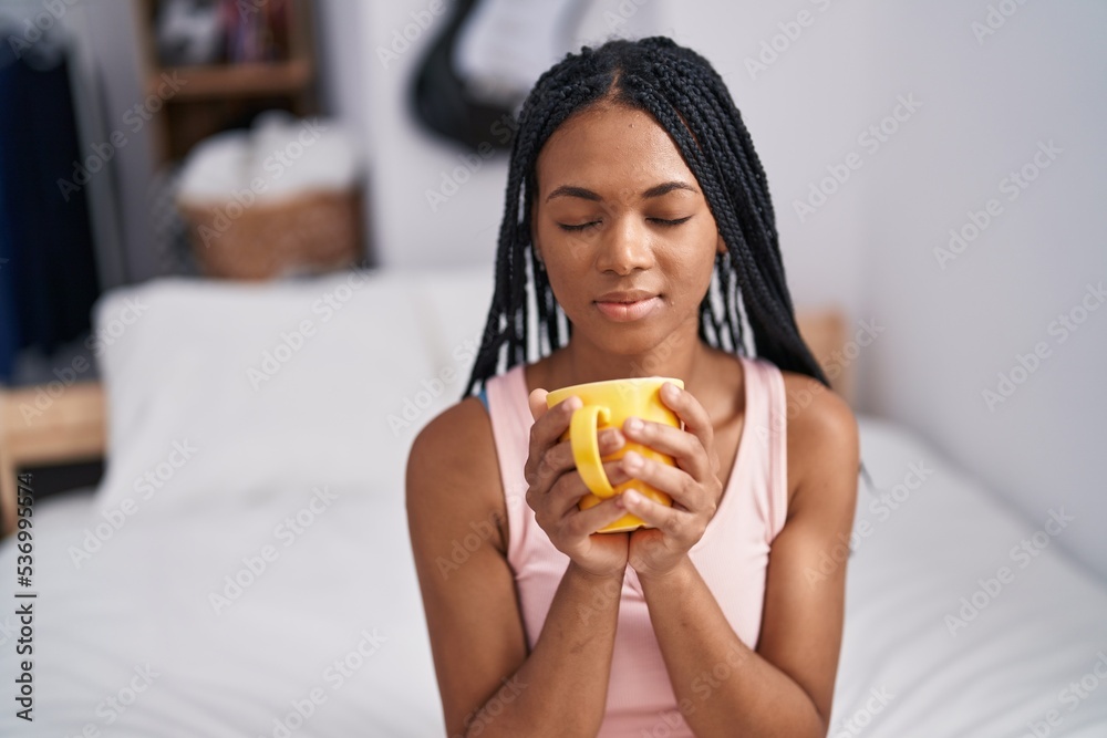African american woman drinking cup of coffee sitting on bed at bedroom African american woman drinking cup of coffee sitting on bed at bedroom