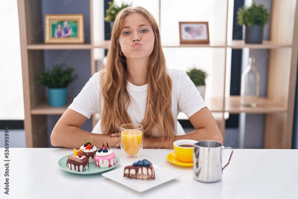 Young caucasian woman eating pastries t for breakfast puffing cheeks with funny face. mouth inflated with air, crazy expression.