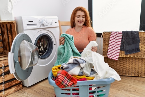 Young redhead woman cleaning clothes using washing machine at laundry room