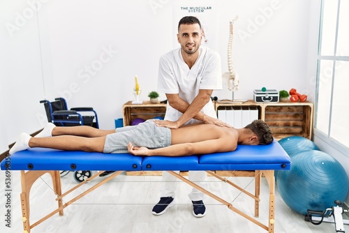 Two hispanic men physiotherapist and patient having rehab session massaging back at clinic