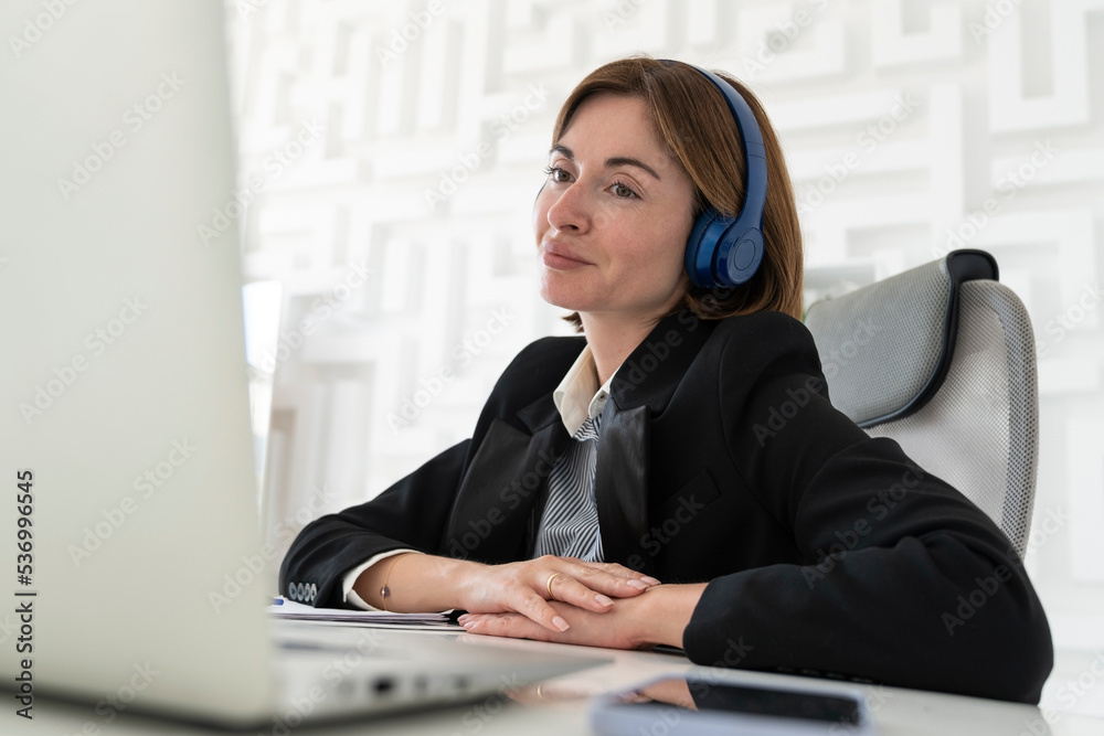 Thoughtful business woman in headphones working on laptop and listening to business class in the office. Distance work and online education concept Thoughtful business woman in headphones working on laptop and listening to business class in the office. Distance work and online education concept