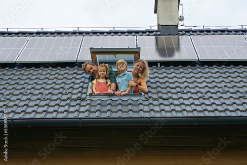 Bilde på lerret Happy family leaning out from skylight window in their new house with solar panels on the roof