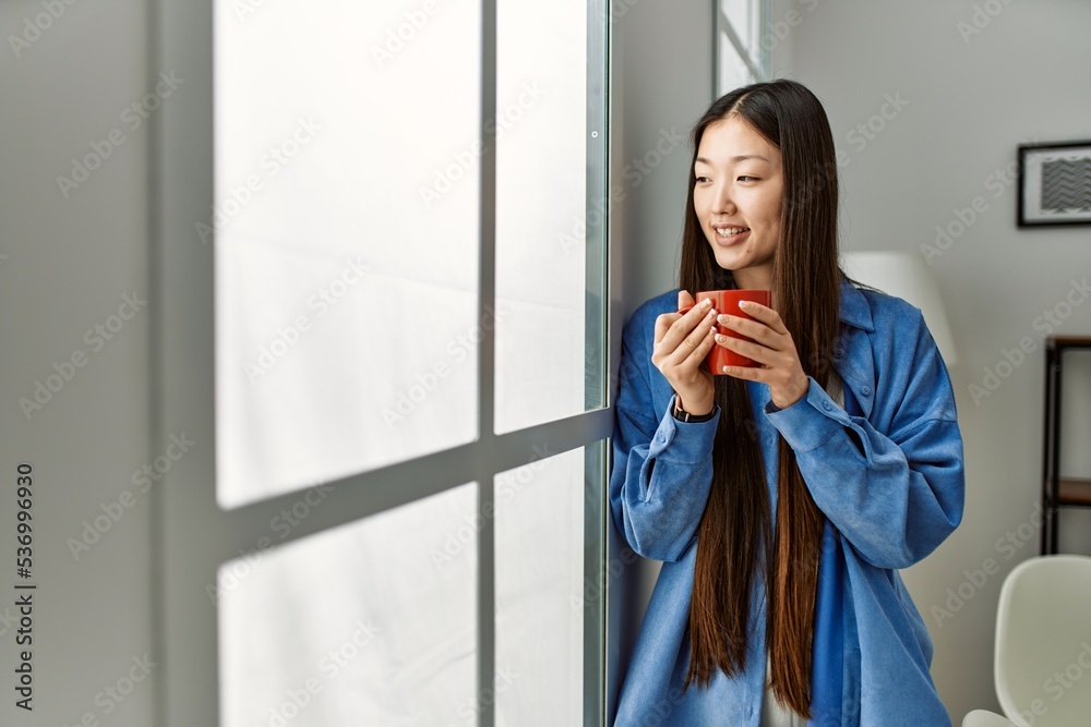 Fototapeta premium Young chinese girl drinking coffee standing at home.