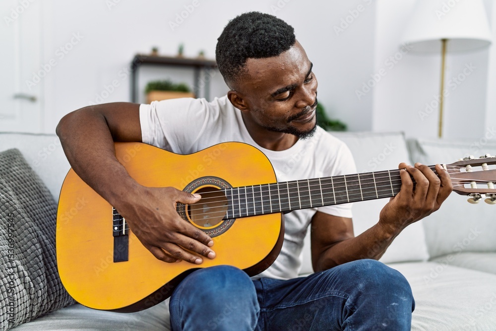 Young african american man smiling confident playing guitar at home