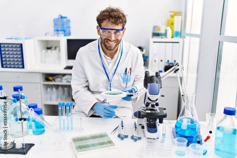 Young hispanic man wearing scientist uniform using loupe at laboratory Young hispanic man wearing scientist uniform using loupe at laboratory