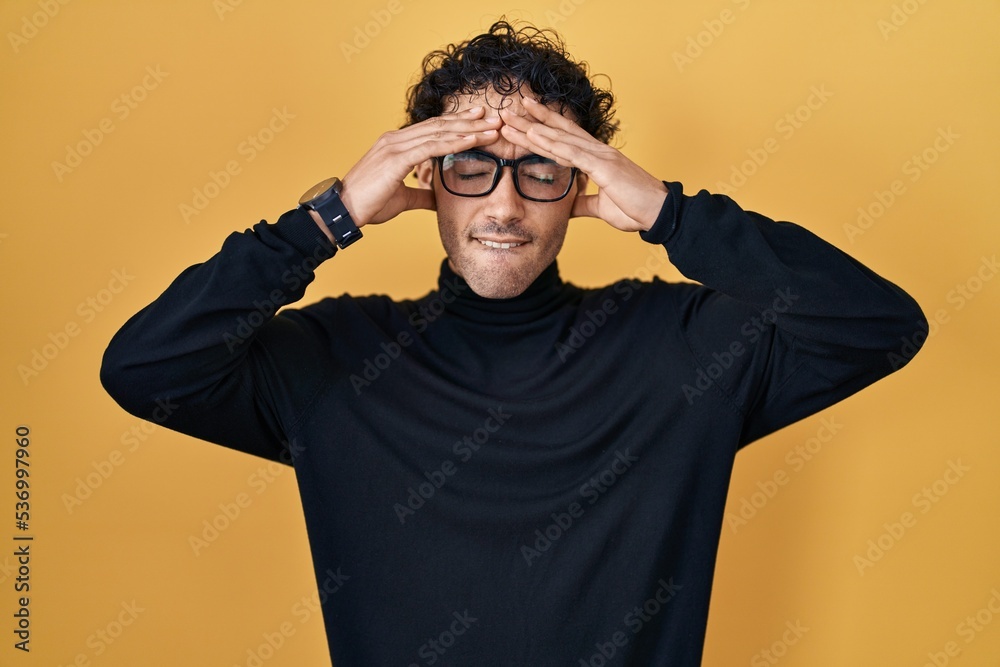 Hispanic man standing over yellow background suffering from headache desperate and stressed because pain and migraine. hands on head. Hispanic man standing over yellow background suffering from headache desperate and stressed because pain and migraine. hands on head.