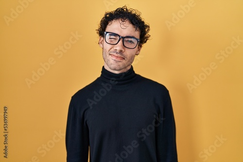 Hispanic man standing over yellow background winking looking at the camera with sexy expression, cheerful and happy face. © Krakenimages.com