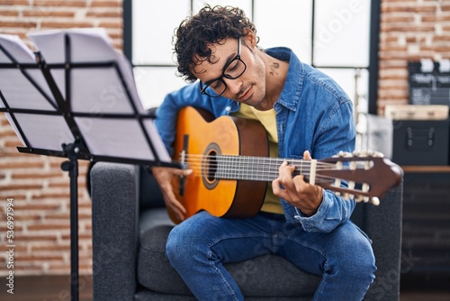 Young hispanic man musician playing classical guitar at music studio