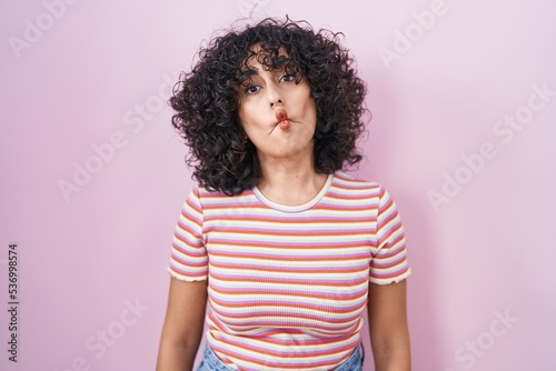 Young middle east woman standing over pink background making fish face with lips, crazy and comical gesture. funny expression. © Krakenimages.com