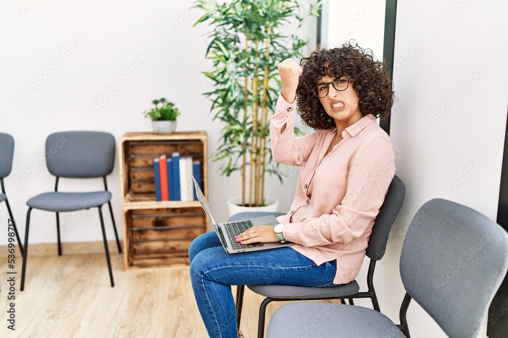 Young middle eastern woman sitting at waiting room working with laptop annoyed and frustrated shouting with anger, yelling crazy with anger and hand raised Young middle eastern woman sitting at waiting room working with laptop annoyed and frustrated shouting with anger, yelling crazy with anger and hand raised