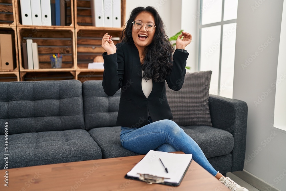 Young asian woman at consultation office celebrating crazy and amazed for success with arms raised and open eyes screaming excited. winner concept Young asian woman at consultation office celebrating crazy and amazed for success with arms raised and open eyes screaming excited. winner concept