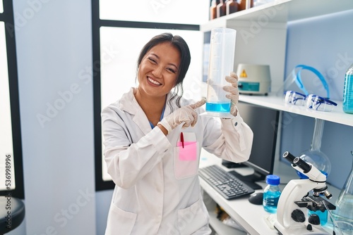Young chinese woman wearing scientist uniform measuring liquid at laboratory