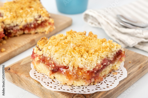 Portion of crumbly shortbread pie with plum and apple jam on wooden board. Dessert with fruit and streusel.