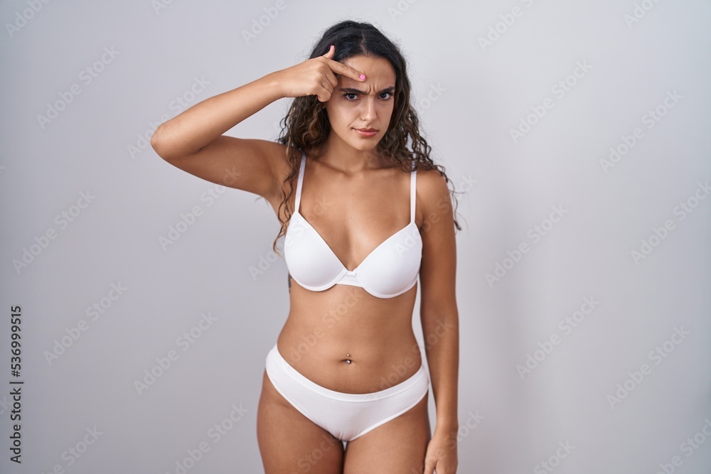 Fototapeta premium Young hispanic woman wearing white lingerie pointing unhappy to pimple on forehead, ugly infection of blackhead. acne and skin problem
