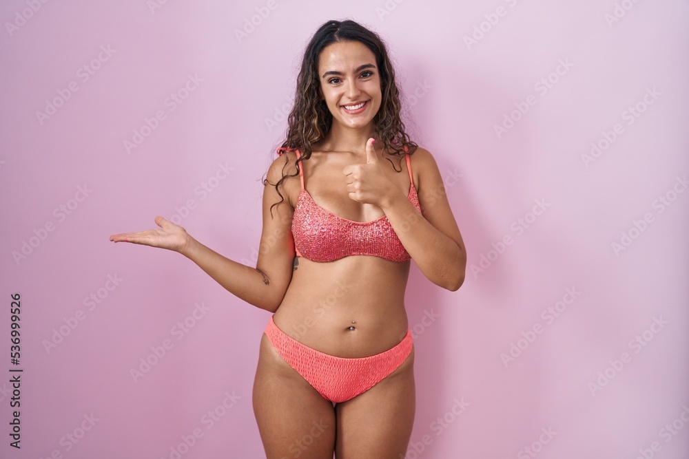 Young hispanic woman wearing lingerie over pink background showing palm hand and doing ok gesture with thumbs up, smiling happy and cheerful Young hispanic woman wearing lingerie over pink background showing palm hand and doing ok gesture with thumbs up, smiling happy and cheerful