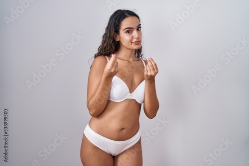 Young hispanic woman wearing white lingerie doing money gesture with hands, asking for salary payment, millionaire business