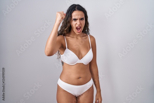 Young hispanic woman wearing white lingerie angry and mad raising fist frustrated and furious while shouting with anger. rage and aggressive concept. © Krakenimages.com