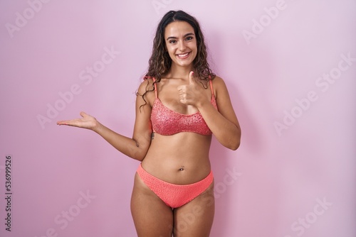 Young hispanic woman wearing lingerie over pink background showing palm hand and doing ok gesture with thumbs up, smiling happy and cheerful