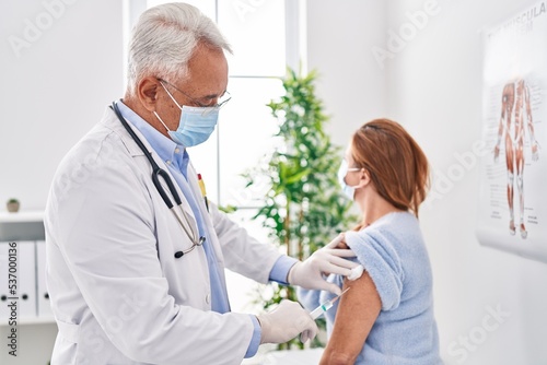 Middle age man and woman doctor wearing medical mask vaccinating patient at clinic