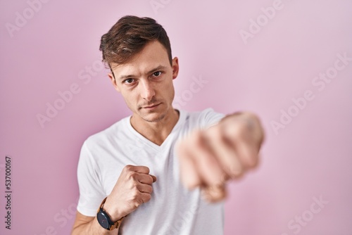 Caucasian man standing over pink background punching fist to fight, aggressive and angry attack, threat and violence © Krakenimages.com