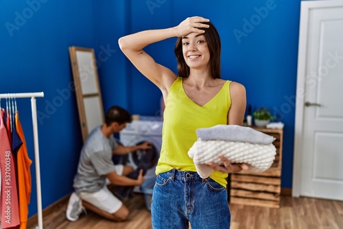 Young brunette woman holding folded laundry stressed and frustrated with hand on head, surprised and angry face