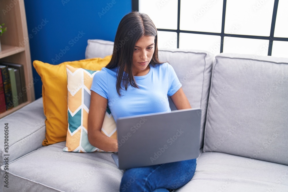 Young beautiful hispanic woman using laptop sitting on sofa at home Young beautiful hispanic woman using laptop sitting on sofa at home
