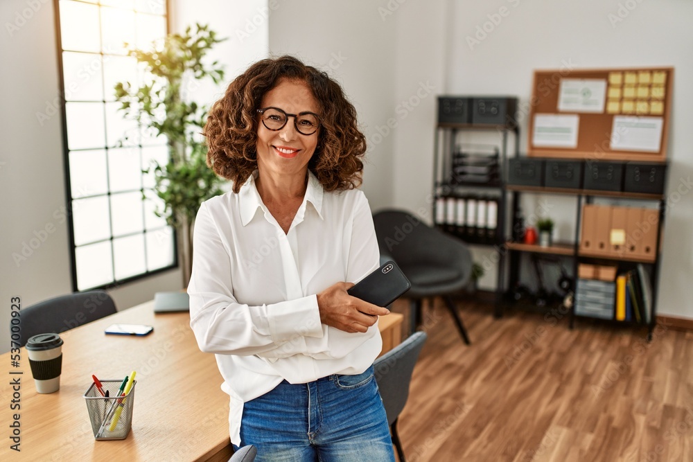 Middle age hispanic woman smiling confident holding smartphone at office Middle age hispanic woman smiling confident holding smartphone at office