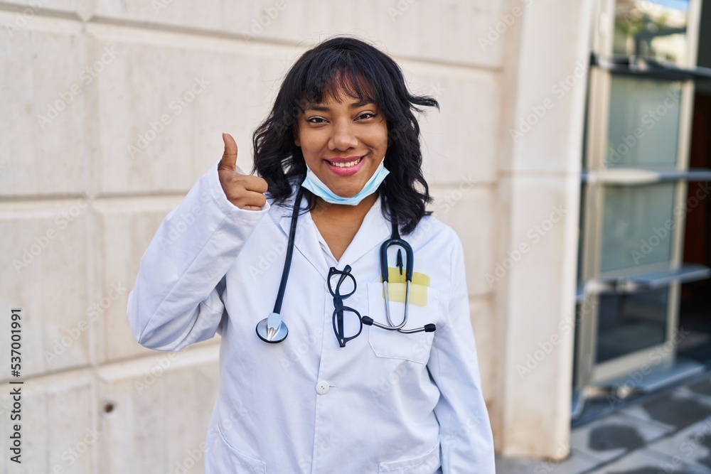 Hispanic doctor woman wearing stethoscope outdoors smiling happy and positive, thumb up doing excellent and approval sign Hispanic doctor woman wearing stethoscope outdoors smiling happy and positive, thumb up doing excellent and approval sign