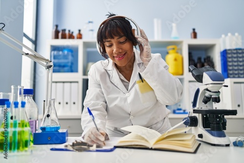 Young beautiful latin woman scientist listening to music working at laboratory