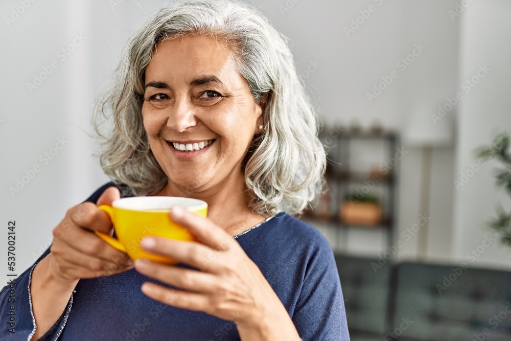 Middle age grey-haired woman drinking coffee standing at home. Middle age grey-haired woman drinking coffee standing at home.