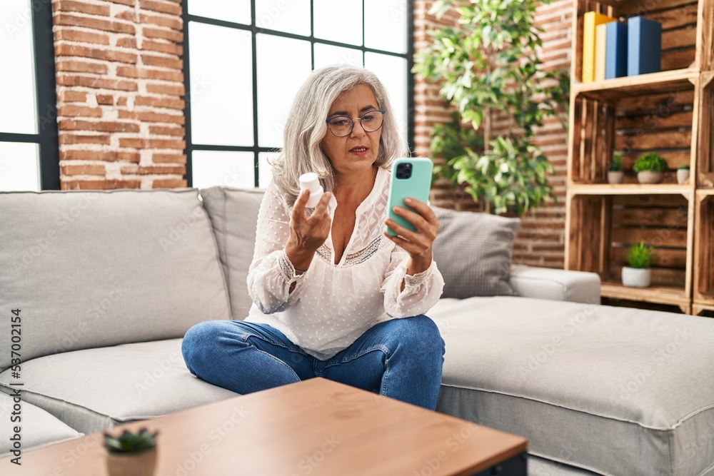 Middle age woman using smartphone holding pills at home Middle age woman using smartphone holding pills at home