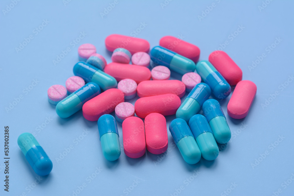 Pink pills and blue capsules on blue background.