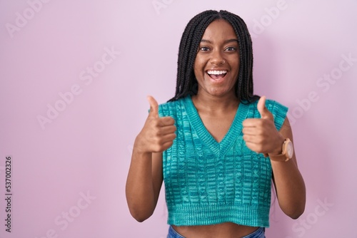 Young african american with braids standing over pink background success sign doing positive gesture with hand, thumbs up smiling and happy. cheerful expression and winner gesture.