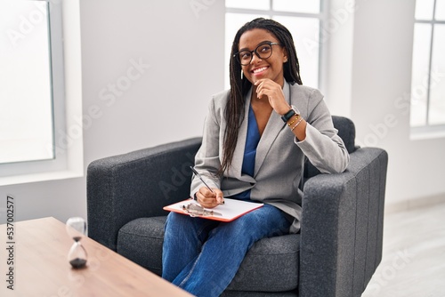 Young african american with braids working at consultation office with hand on chin thinking about question, pensive expression. smiling and thoughtful face. doubt concept.