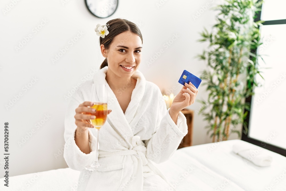 Young hispanic woman holding credit card drinking champagne at beauty center. Young hispanic woman holding credit card drinking champagne at beauty center.
